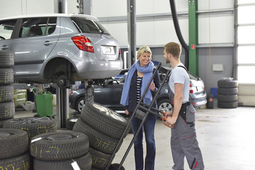 Car mechanic with client and tires in workshop