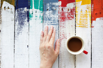 Fototapeta na wymiar woman hand with coffee cup on grunge colorful wooden panel