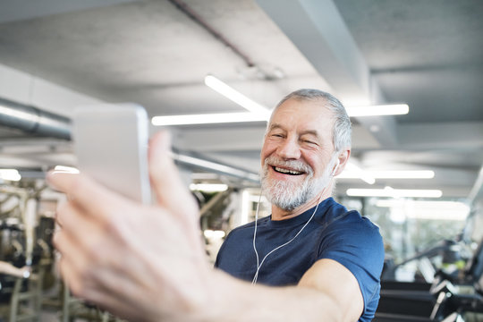 Happy senior man with smartphone and earphones in gym