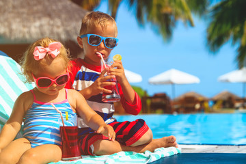 Obraz na płótnie Canvas little boy and toddler girl drinking juices on beach