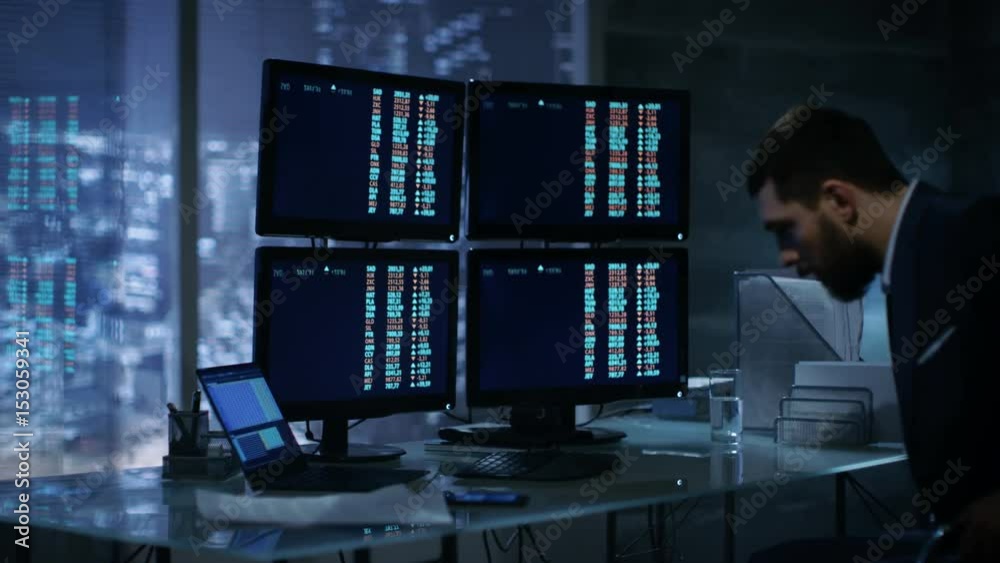 Aufkleber traders takes place at his desk and starts working with numbers showing on multiple displays. shot o