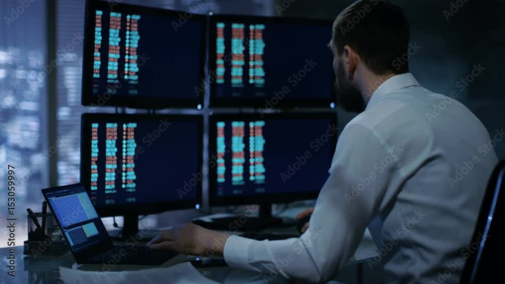 Poster Late at Night Trader Reads Numbers on His Multiple Displays with Stock Information on Them. In Background Big City Window View. Shot on RED EPIC-W 8K Helium Cinema Camera.