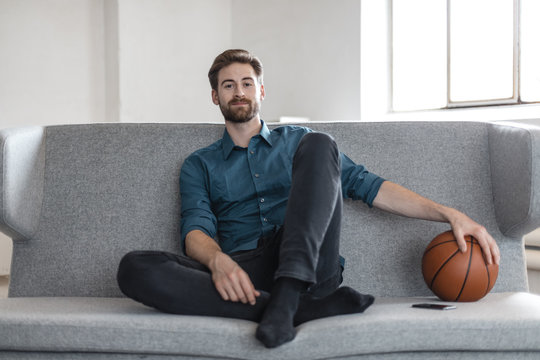 Portrait of relaxed young man sitting on couch with basketball - Powered by Adobe