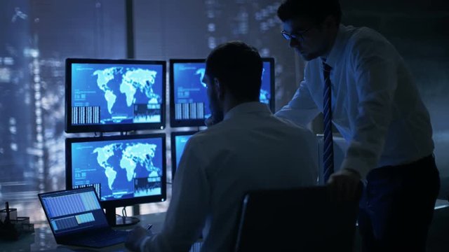 Late at Night in Office Building Security Service Men Have Discussion while  Attentively Observing Monitors with Location Sensitive Information Shown on Them. Shot on RED EPIC-W 8K Helium Camera