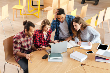 Sad confused students sitting in library using laptop computer.