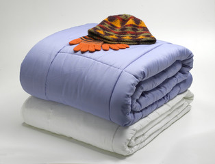 folded duvets/quilts with wool hat and gloves on top, isolated on white