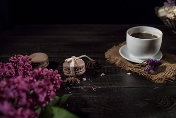 Obraz na płótnie Canvas White cup with coffee on a linen napkin and old wooden table and stack of macarons. 