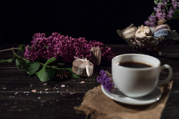 Coffee and cream macarons with cup of coffee and lilac on background