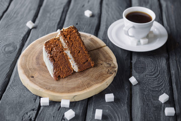 Piece of homemade cake and coffee on a black wooden table. Biscuit cake with black coffee. Lump sugar scattered on a table.