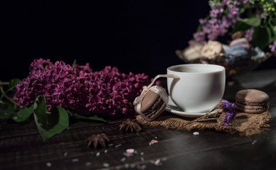 Coffee and cream macarons with cup of coffee and lilac on background