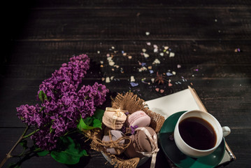 Coffee and cream macaroons in a white plate with coffee cup, eco notebook with a pencil and lilac branch in the centre of a picture.