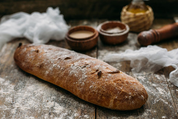 Close up view of fresh brown crispy loaf of bread lying on the wooden table sprinkled with flour.