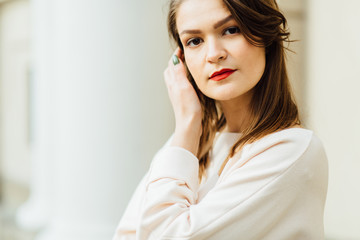 Close up portrait of elegant woman with red lips in a beige blouse on the white building background.