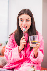 Portrait of young sick woman who keeps cup of water and takes medicine at home