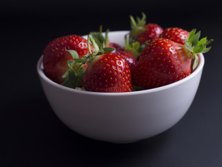 Fresh, red, ripe strawberries in white bowl isolated on black background