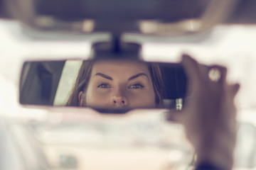 Young woman looks in the car rearview mirror and holds it by hand
