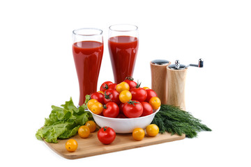 Still life of red and yellow tomatoes and two cups of tomato juice on a white background.