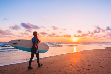 Fototapeta na wymiar Surf girl with long hair go to surfing. Woman with surfboard on a beach at sunset or sunrise. Surfer and ocean
