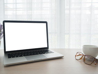 wood office table with blank screen laptop for text, modern eyeglasses and white coffee cup on beautiful white drape window texture background.