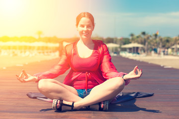Fototapeta na wymiar Woman sitting in yoga asana lotus pose on the wooden pier