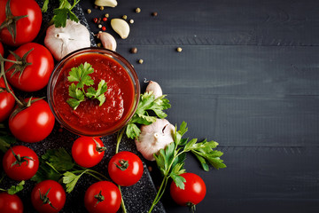Still life with tomatoes, garlic, parsley, tomato sauce and pepper on black wooden boards.
