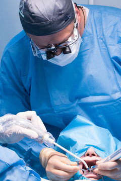 A male dentist in uniform perform dental implantation operation on a patient at dentistry office.