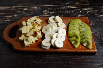 Sliced fresh fruit on a wooden board. Kiwi, banana, apple slices on the board.