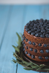 Fototapeta na wymiar chocolate layered cake with blueberries with chocolate cream on a blue wooden background in a brown ceramic plate close-up copyspace