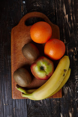 Fresh fruits on a board on a wooden background. View from above. Banana, orange, kiwi, apple. Useful fruits.