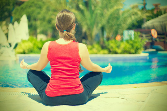 Young woman meditates in yoga asana near the swimpool toned