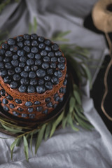 a beautiful cake decorated with blueberries and eucalyptus on ceramic brown plate on the kitchen towel grey on a black background food photo close-up