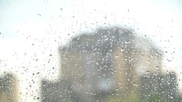 Rainy day, rain drops on the window, dull residential building and some trees in the background out of focus