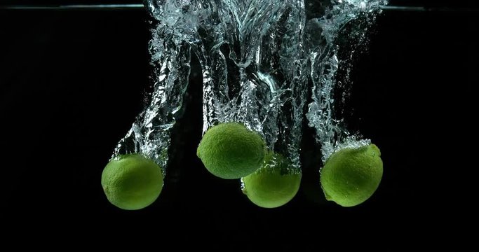 Green Lemons, citrus aurantifolia, Fruits falling into Water against Black Background, Slow Motion 4K