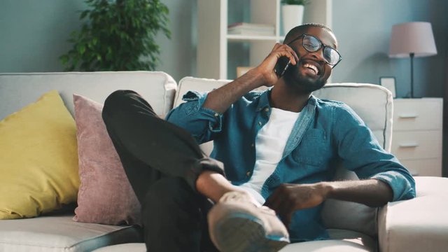Attractive african man celling on the phone while sitting on the sofa at living room. Young man using smart phone for chating.