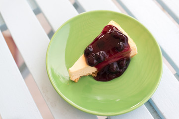 A piece of blueberry cheese pie on green dish with white wooden table.