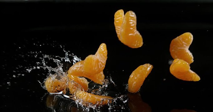 Clementines, citrus reticulata, Fruits falling on Water against black Background, Slow Motion 4K