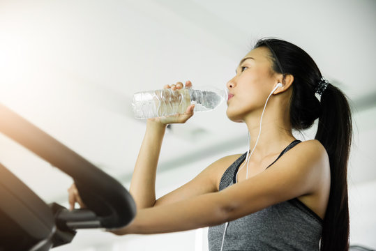 Asian woman in sportswear drinking water after workout at the gym.