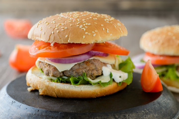 Burger with tomatoes. Fresh hamburger closeup on wooden rustic table.