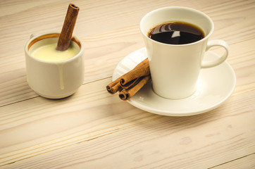 white cup of coffee with cinnamon and condensed milk/cup of black coffee and cup of condensed milk