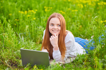 Smiling girl with laptop on grass