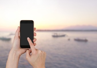 Hand Touching phone next to sea landscape