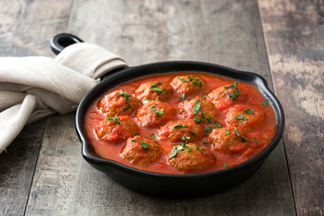 Meatballs with tomato sauce in iron frying pan on wooden table