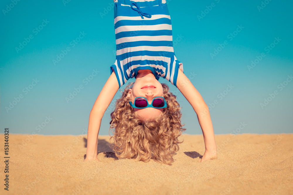 Wall mural Funny child standing upside down on sandy beach