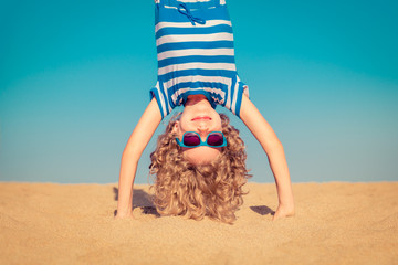 Funny child standing upside down on sandy beach