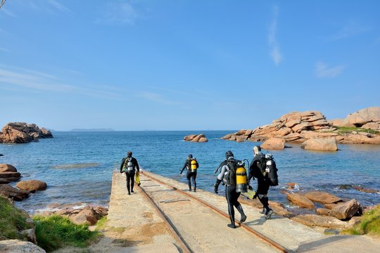 Quatre plongeurs en combinaison descendent dans l'eau pour un entra&icirc;nement &agrave; Ploumanach