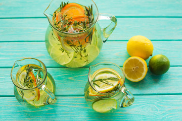 On a bright turquoise wooden surface there are decanters with detox lemonade, lemon, orange, lime,...