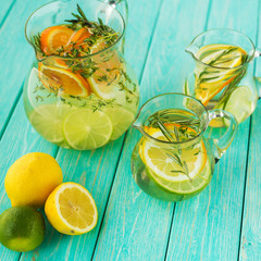On the turquoise wooden surface there are decanters with detox lemonade, lemon, orange, lime,...