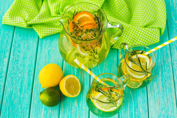 On a bright turquoise wooden surface there are decanters with detox lemonade, lemon, orange, lime, thyme, delicious healthy food, diet, lifestyle, top view