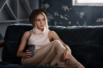 Fashionable beautiful young girl sits on the couch with a glass of fresh coffee in a cozy atmosphere
