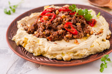 Creamy hummus with spicy mutton minced meat in clay bowl on stone background. Ramadan food.